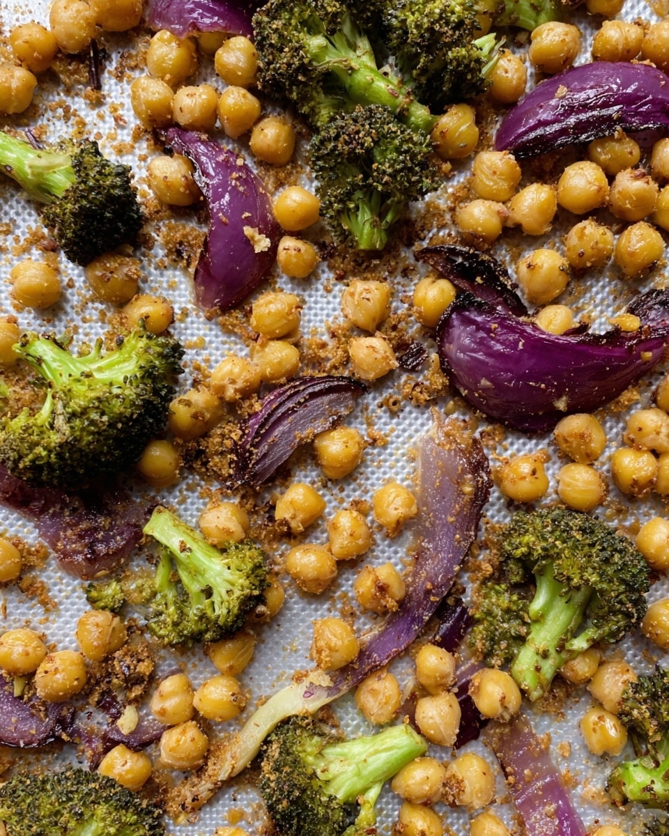 This image shows a close-up of roasted chickpeas, broccoli florets, and red onion slices spread out on a textured white baking mat. The chickpeas are golden yellow with a light crunchy coating, while the broccoli pieces are bright green with some charred black edges. The red onion slices are deep purple and slightly caramelized with a soft texture. The ingredients look evenly mixed and well-roasted with some spice or seasoning powder scattered across them. The background is a white marbled texture. photo taken with an iphone --ar 4:5 --v 7