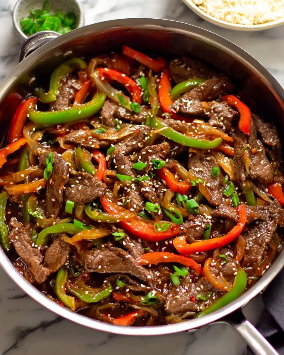 A stainless steel pan filled with a stir-fry dish featuring thin slices of brown beef mixed with strips of red and green bell peppers. The beef and peppers are coated in a glossy dark brown sauce. The dish is topped with small pieces of green onions and white sesame seeds scattered evenly across the surface. The pan is placed on a white marbled surface with a glimpse of a white bowl containing rice in the upper right corner. Photo taken with an iphone --ar 4:5 --v 7