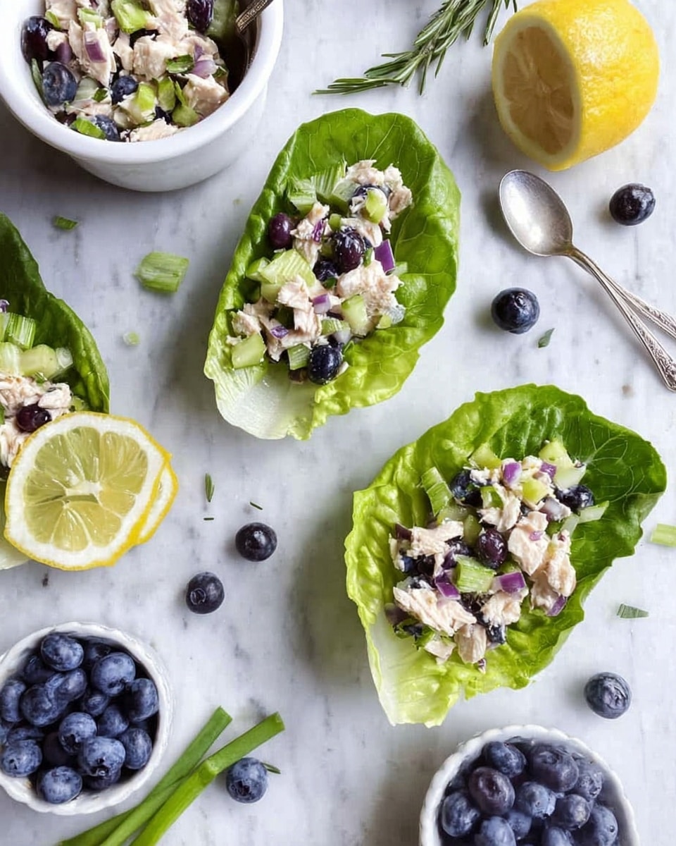 Two fresh green lettuce leaves lie on a white marbled surface, each topped with a mix of chopped light-colored chicken, dark blueberries, small green celery pieces, and tiny bits of purple onion. Around them are scattered whole blueberries and thin lemon slices. In the background, there is a white bowl filled with the same salad, and a small white bowl full of blueberries. Green onion stalks and a sprig of rosemary add a touch of green to the scene. A silver spoon rests on the white marbled surface near a lemon wedge. The overall look is fresh, light, and colorful. photo taken with an iphone --ar 4:5 --v 7