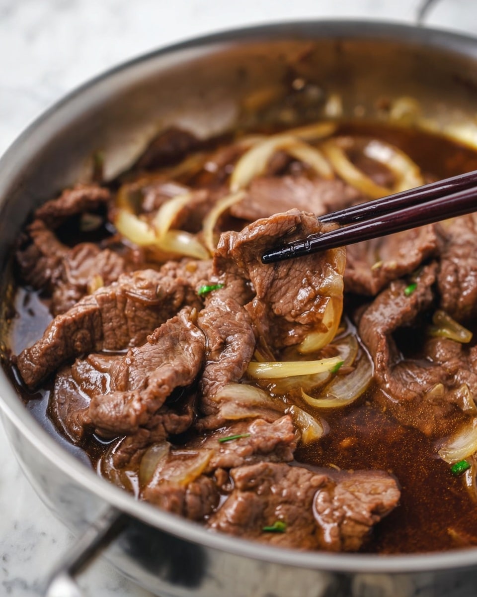 The image shows a silver pan filled with thin brown slices of cooked meat that have a soft and slightly wrinkled texture. The meat is sitting in a glossy, dark brown sauce that looks rich and flavorful. Inside the pan, there are light yellow, translucent slices of cooked onion scattered among the meat. A pair of dark brown chopsticks is holding up one piece of the meat, showing its curl and tender texture. The background is a white marbled surface, and the photo looks clear and close, highlighting the details of the meat and onions photo taken with an iphone --ar 4:5 --v 7
