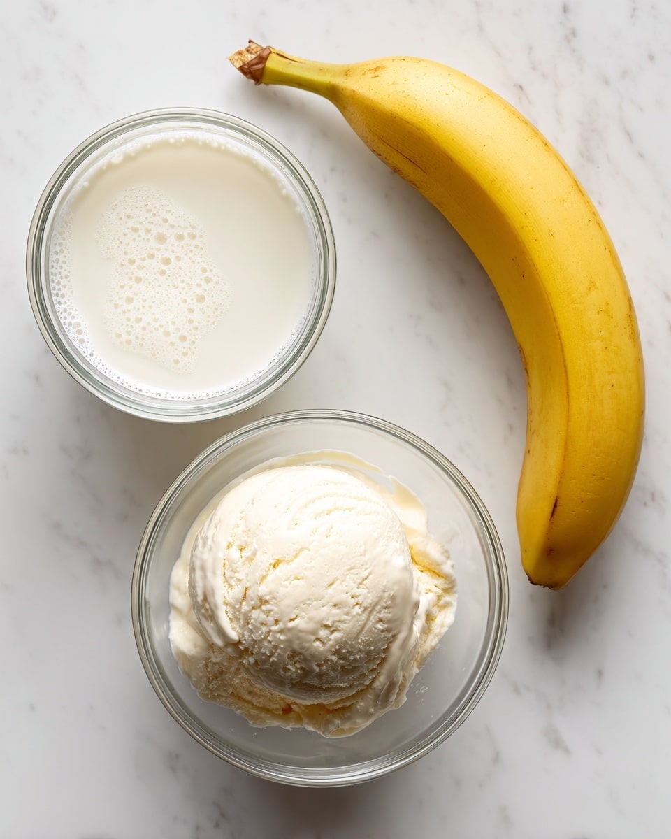 A clear glass bowl on a white marbled surface holds a scoop of creamy, white vanilla ice cream with a smooth texture and slight melting around the edges. Near it, a clear glass bowl filled with smooth white milk shows small bubbles on its surface. Above the bowls lays a whole ripe yellow banana with a slightly curved shape and a pale brown tip on one end. The three items are spaced apart on the white marbled surface. Photo taken with an iphone --ar 4:5 --v 7