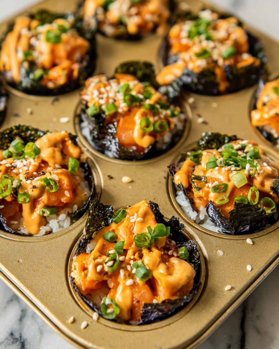 This image shows a close-up of a muffin tray filled with small baked bites. Each piece has a crispy dark green seaweed layer forming the cup, filled with white rice as the base layer. On top, there are orange chunks of cooked salmon, drizzled with a creamy orange sauce. The bites are sprinkled with chopped green onions and white sesame seeds, adding a fresh green and white contrast. The muffin tray is gold-colored and placed on a white marbled surface. The photo taken with an iphone --ar 4:5 --v 7