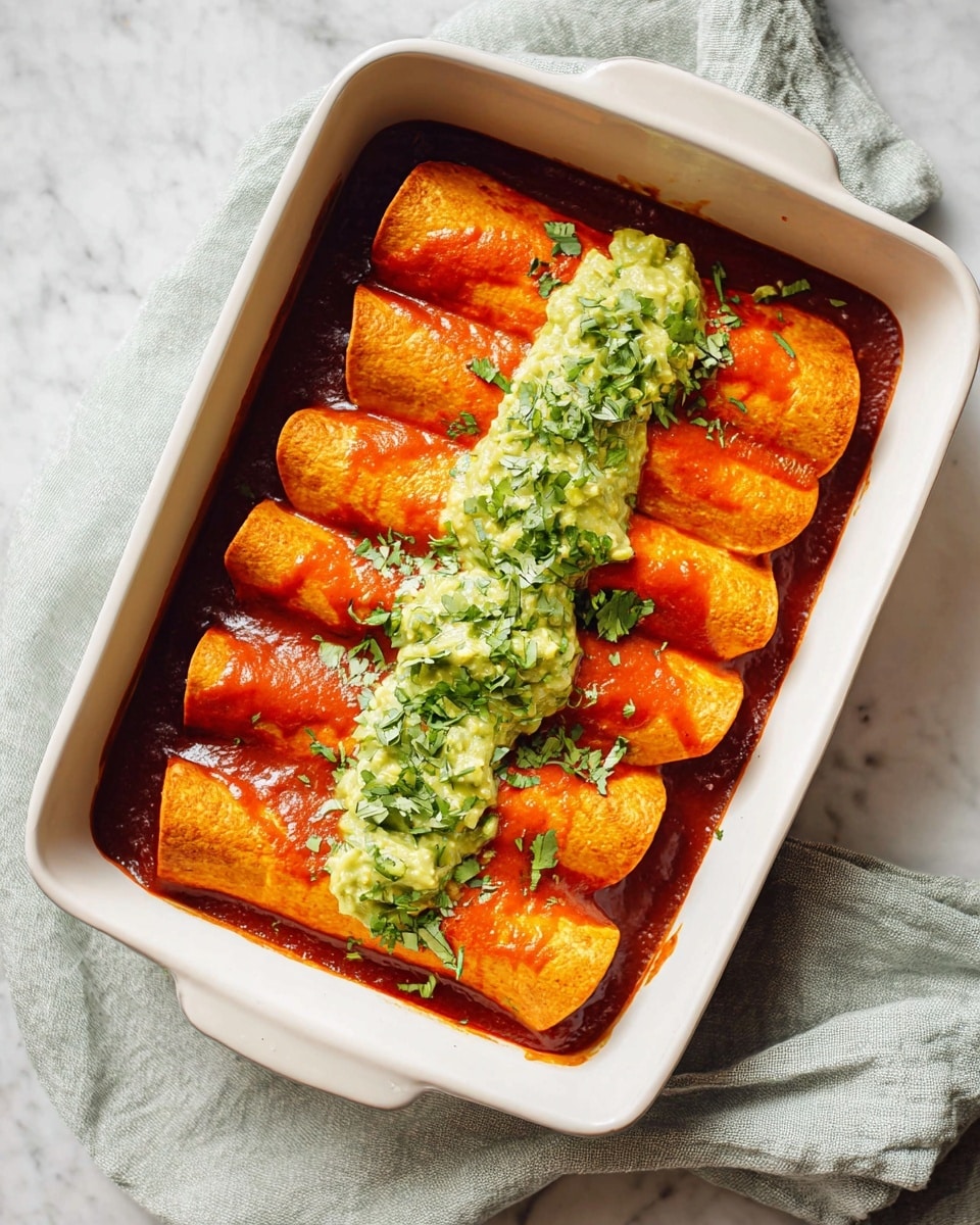 A white rectangular dish holds six rolled orange tortillas lined up in two rows of three, each covered with a smooth red sauce that slightly pools at the bottom. On top of the tortillas, there is a line of green creamy guacamole spread finely across the center. Fresh chopped green herbs are sprinkled over the guacamole and tortillas adding contrast. The dish rests on a white marbled textured surface with a folded light gray-green cloth beside it. photo taken with an iphone --ar 4:5 --v 7