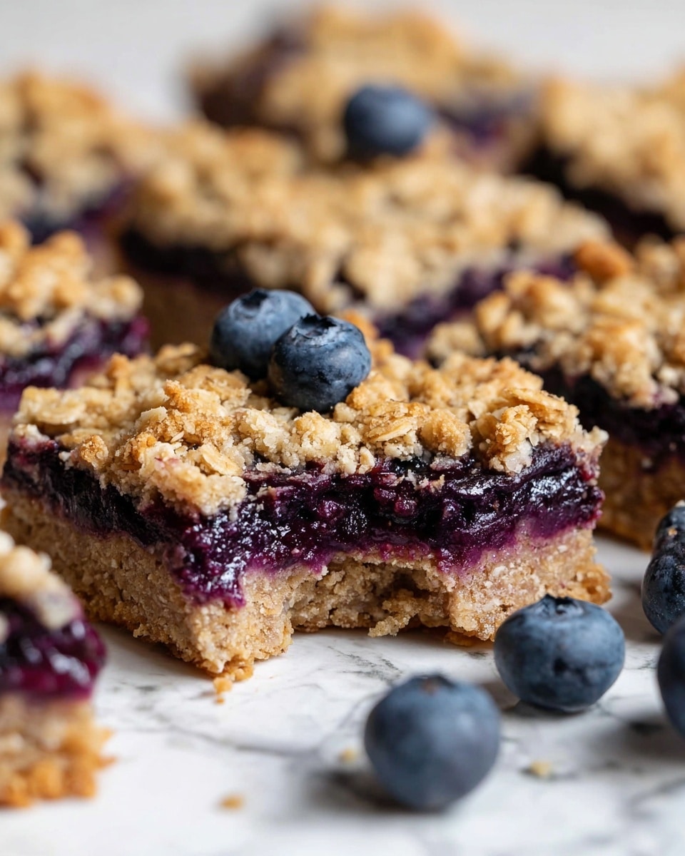 The image shows a close-up of several square blueberry oat bars placed on a white marbled surface. Each bar has two visible layers: a bottom layer of soft, light brown oat crust and a thick middle layer filled with dark purple blueberry jam. The top layer is a crumbly oat topping with a golden-brown color and a rough texture. Some fresh blueberries are placed around the bars for decoration. One bar in the center has a bite taken out, showing the juicy blueberry filling clearly. Photo taken with an iphone --ar 4:5 --v 7