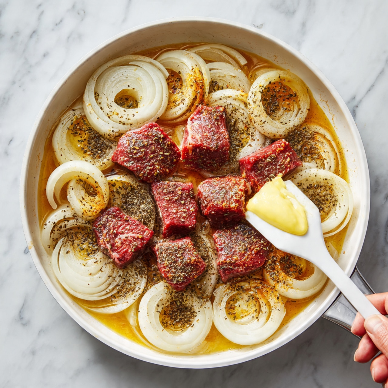 In a white pan on a white marbled surface, thinly sliced onions are light brown and soft, spread evenly across the pan base; a woman's hand holds a white spatula adding a dollop of light yellow butter to the onions in the first layer. The second layer shows chunks of raw red meat with white marbling placed on top of the cooked onions, in the center of the pan. The third layer keeps the meat, now slightly browned, covered with bright yellow and dark brown spices sprinkled all over, resting on the onions. The final layer shows the meat, onions, and spices combined and simmering in a golden brown liquid with some steam, filling the pan in a warm, rich sauce. Photo taken with an iphone --ar 4:5 --v 7