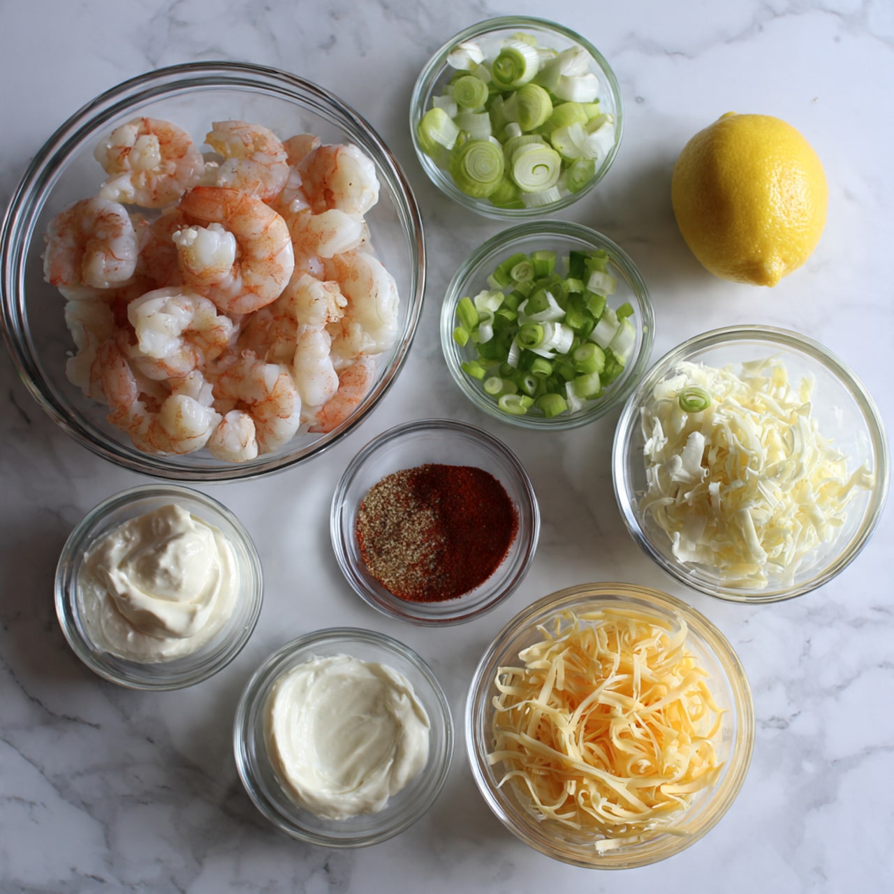 The image shows several small clear glass bowls arranged on a white marbled surface. The largest bowl at the top center contains cooked shrimp with a pink and white color. Around it, other bowls contain different ingredients: a bowl of light green chopped green onion to the upper right, a tiny bowl with reddish Old Bay seasoning in the center, another bowl on the middle left holding white cream cheese, a bowl with off-white sour cream below the cream cheese, a small bowl of light beige mayonnaise to the right of sour cream, and a bowl filled with pale yellow shredded cheddar cheese at the bottom right. There is also a half lemon with a bright yellow color placed near the bottom left and a tiny bowl with dark red hot sauce near the bottom center. The photo is taken with an iphone --ar 4:5 --v 7
