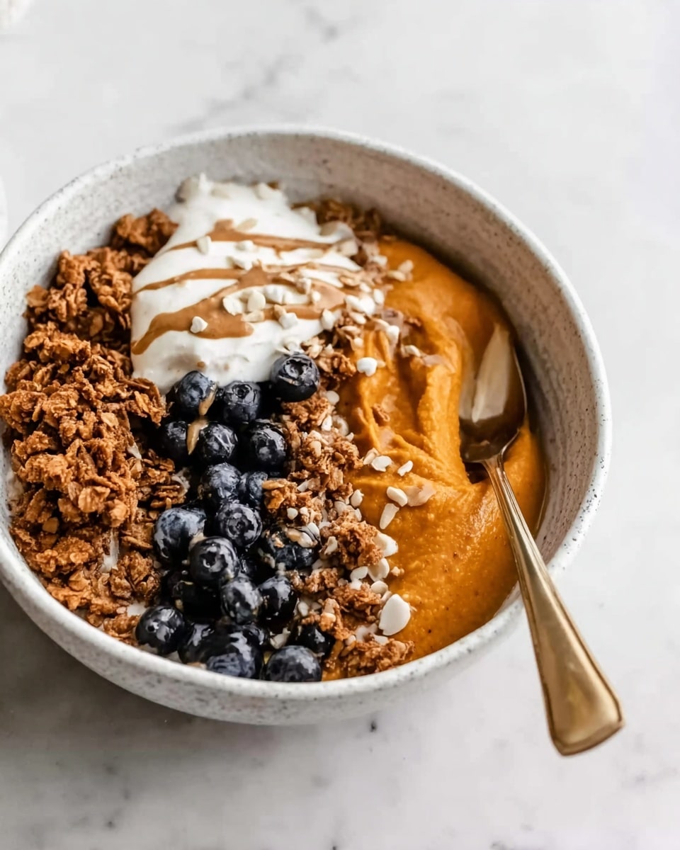 A white bowl with a textured surface holds a layered dish starting with a thick orange base that looks smooth and creamy, likely sweet potato or pumpkin puree, on the right side. Next to it on the left is a cluster of small dark blue blueberries, creating a strong color contrast. Below the blueberries, there is a crunchy layer of granola, brown with a rough texture, sprinkled unevenly. On the upper left, a dollop of white creamy yogurt sits partially on the blueberries and puree, topped with thin drizzles of light brown sauce or nut butter, adding texture and color. Small white seeds or nuts are sprinkled lightly over the entire dish. A silver spoon with a gold handle rests inside the bowl on the right side. The bowl is placed on a white marbled surface. photo taken with an iphone --ar 4:5 --v 7