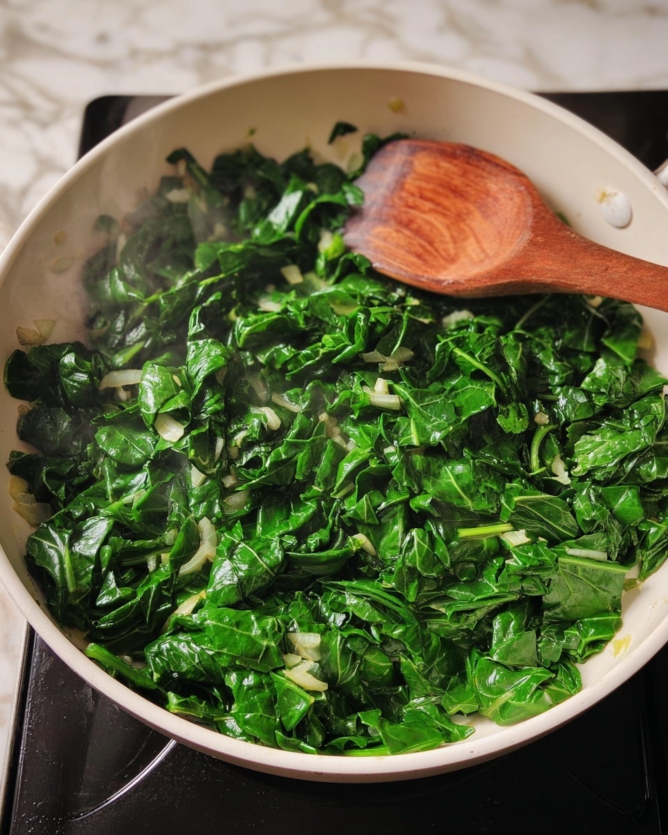A white pan filled with bright green chopped leafy vegetables being cooked, with small pieces of light onion mixed in. A wooden spoon rests on top of the greens inside the pan, which is on a dark stovetop. The background shows a white marbled textured surface near the pan. Steam rises slightly from the cooked greens, showing heat and cooking. Photo taken with an iphone --ar 4:5 --v 7
