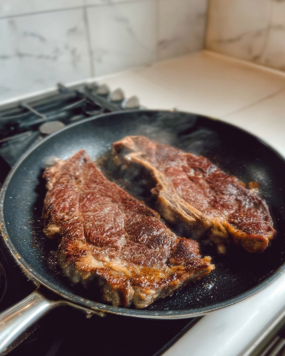 Two large brown cooked steaks with sear marks lie side by side in a black frying pan on a stove. The meat shows a mix of darker charred edges and slightly lighter brown cooked areas, with visible fat marbling on the surface. Steam rises gently from the hot meat. The background is a white marbled kitchen countertop with a white tiled wall behind. Photo taken with an iphone --ar 4:5 --v 7