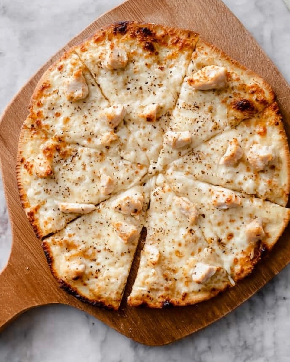 A round flatbread pizza is shown on a wooden board with a handle. It is sliced into eight pieces. The crust is thin and golden brown with darker toasted spots around the edges. The pizza has a light layer of melted cheese with small pieces of light brown cooked chicken scattered evenly on top. Black pepper is sprinkled gently over the whole pizza. The wooden board stands on a white marbled surface. photo taken with an iphone --ar 4:5 --v 7