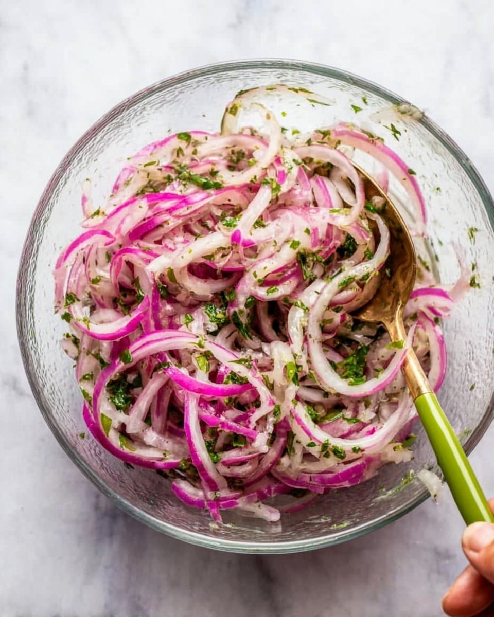 A clear glass bowl filled with thinly sliced purple and white onions mixed with finely chopped green herbs, all coated in a light dressing that gives a slight shine to the onion layers; a woman's hand holds a gold spoon with a green handle resting inside the bowl, all placed on a white marbled surface photo taken with an iphone --ar 4:5 --v 7