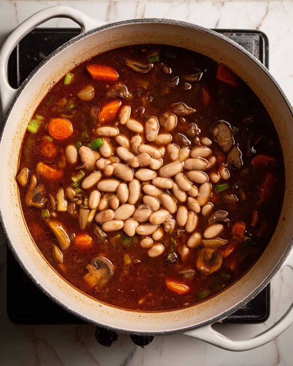 The image shows a top view of a large white pot filled with a dark brown soup or stew. In the center, there is a pile of light beige beans floating on top. Around the beans, the liquid is thick and rich, with visible slices of orange carrots, small pieces of green celery, and chunks of brown mushrooms spread evenly. The pot sits on a stove, and the background is a white marbled surface. The lighting highlights the textures and colors of the ingredients clearly. photo taken with an iphone --ar 4:5 --v 7