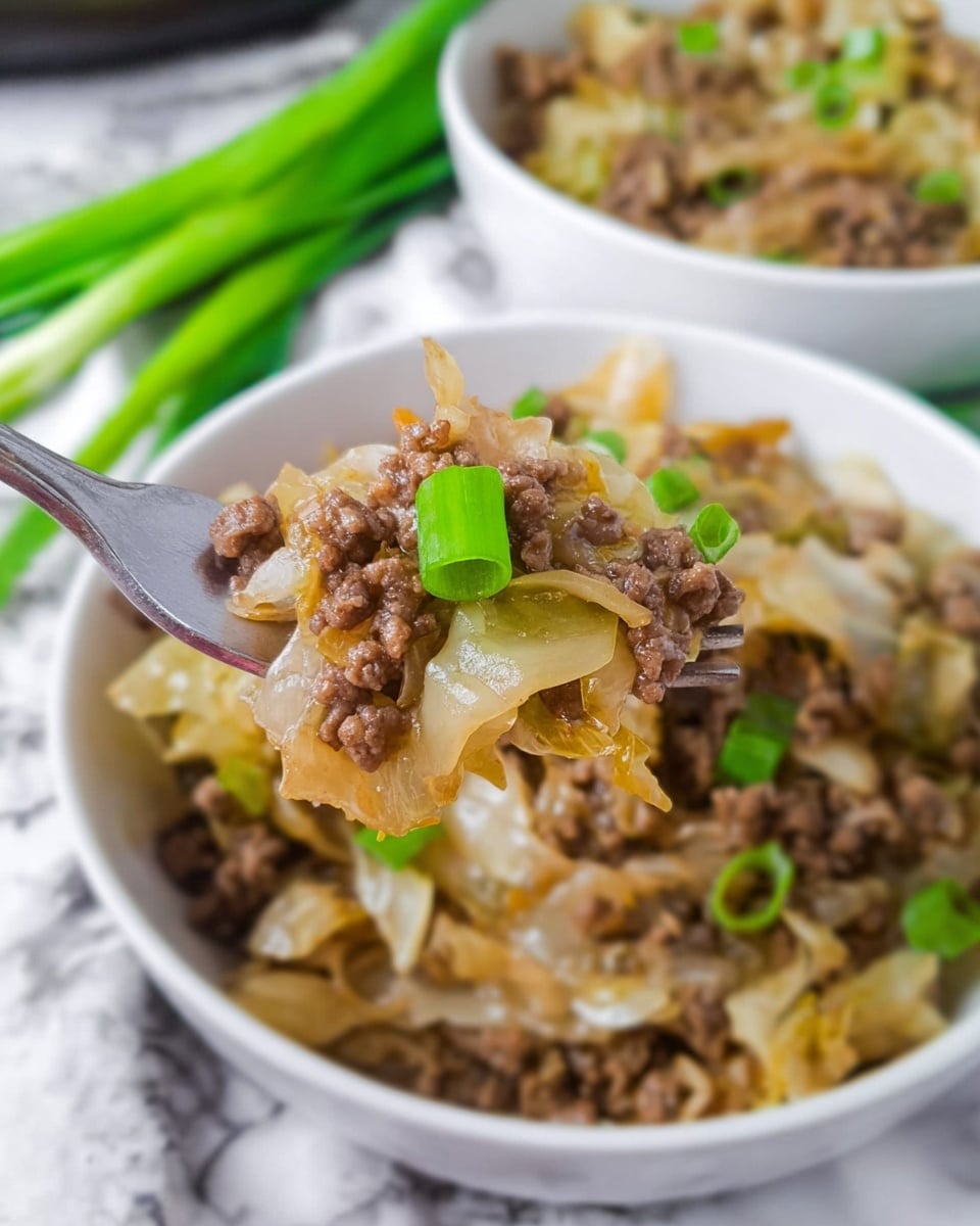 A close-up view of a white bowl filled with cooked ground meat mixed with translucent cooked cabbage pieces, topped with small bright green chopped green onions. A silver fork is lifting a bite showing the layers of minced meat and soft cabbage strands, with a small piece of green onion resting on top. The background includes a second bowl slightly out of focus and some green onions, all set on a white marbled surface. photo taken with an iphone --ar 4:5 --v 7