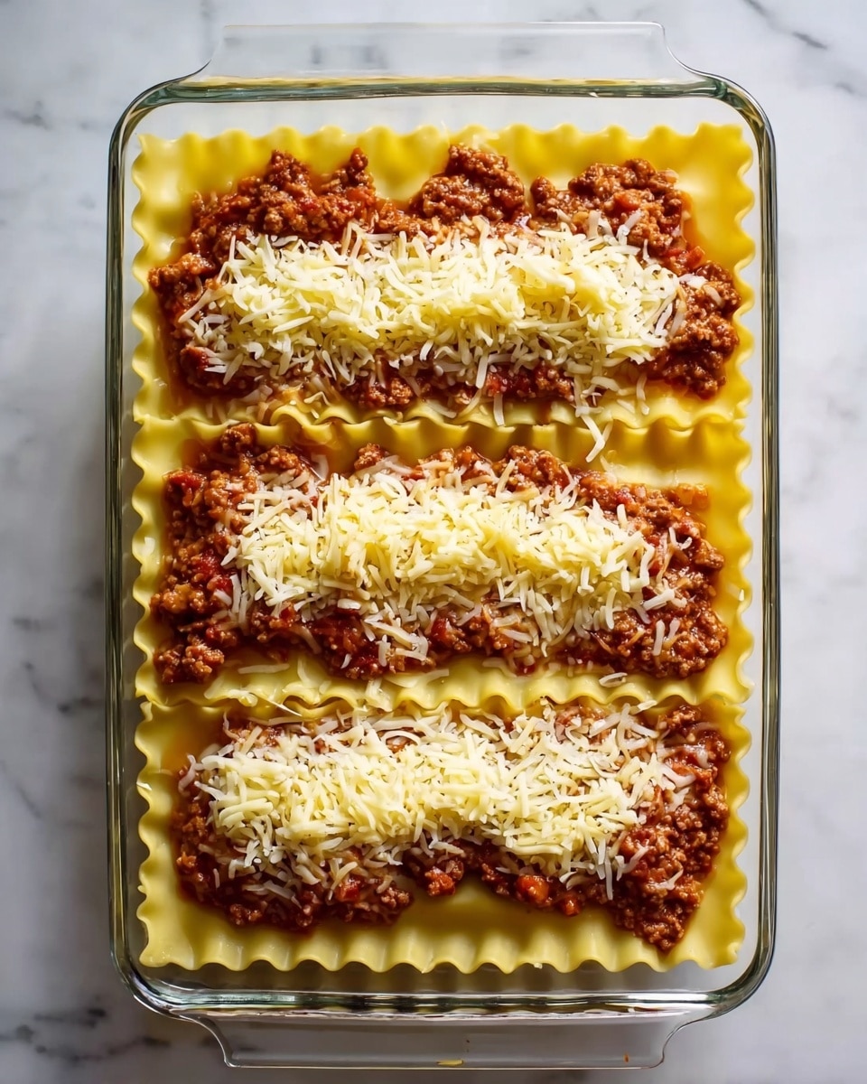 A glass baking dish filled with three visible layers of lasagna arranged horizontally. The bottom layer consists of yellow, wavy-edged pasta sheets. The second layer is a chunky red meat sauce spread evenly across the pasta, with small bits visible throughout. The top layer is shredded white and pale yellow cheese sprinkled generously over the meat sauce, covering it almost completely. The dish sits on a white marbled surface. Photo taken with an iphone --ar 4:5 --v 7