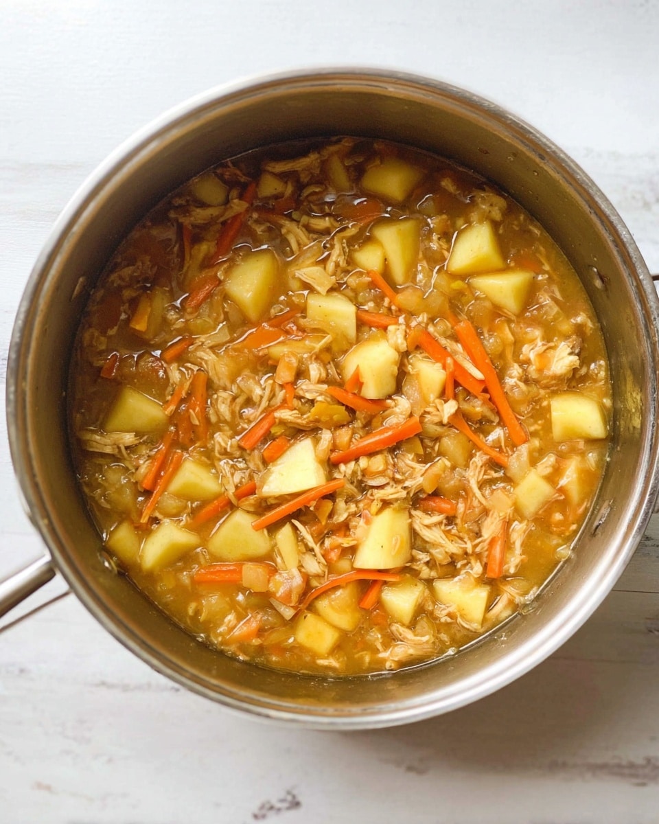 A top view of a silver pot filled with a thick stew-like mixture showing chunks of yellow apples, thin strips of orange carrots, small bits of shredded light brown chicken, and some small grains or oats, all mixed in a light brown, slightly shiny sauce, sitting on a white marbled surface, photo taken with an iphone --ar 4:5 --v 7