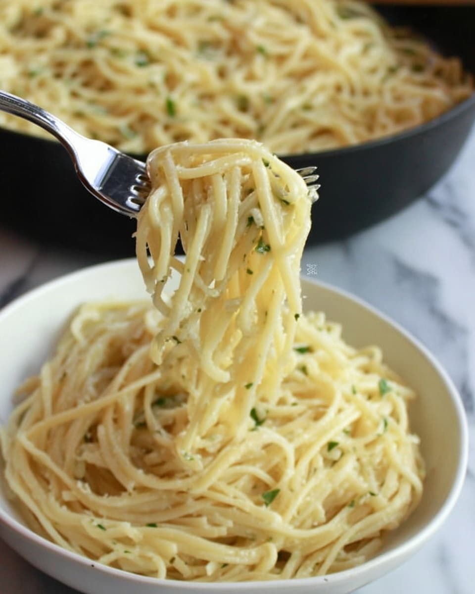 The image shows a close-up of creamy spaghetti pasta with small green herbs mixed in. There are thin pale yellow pasta strands with a smooth texture. A woman's hand is lifting a forkful of pasta out of a white bowl filled with more pasta. In the background, a white pan filled with the same pasta is visible. The setting is on a white marbled surface. photo taken with an iphone --ar 4:5 --v 7