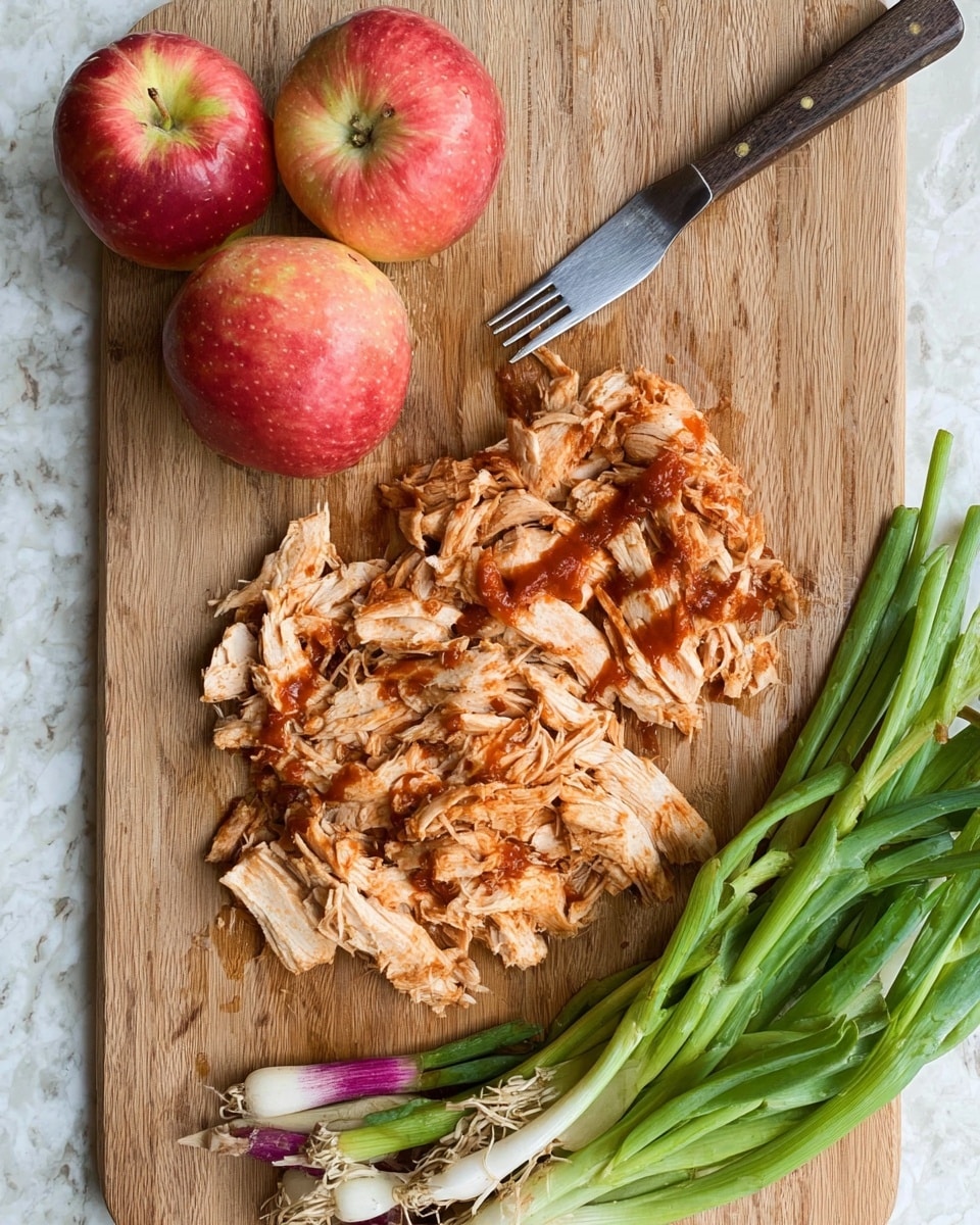 The image shows a wooden cutting board with shredded cooked chicken pieces spread out unevenly in the center, topped with a reddish-brown sauce. To the right of the chicken, there is a bundle of fresh green onions with white and purple roots still attached. On the upper left side of the board, two red apples with yellow patches are placed close together. A fork with a dark handle rests horizontally on the board above the chicken pieces. The background is a white marbled surface. photo taken with an iphone --ar 4:5 --v 7