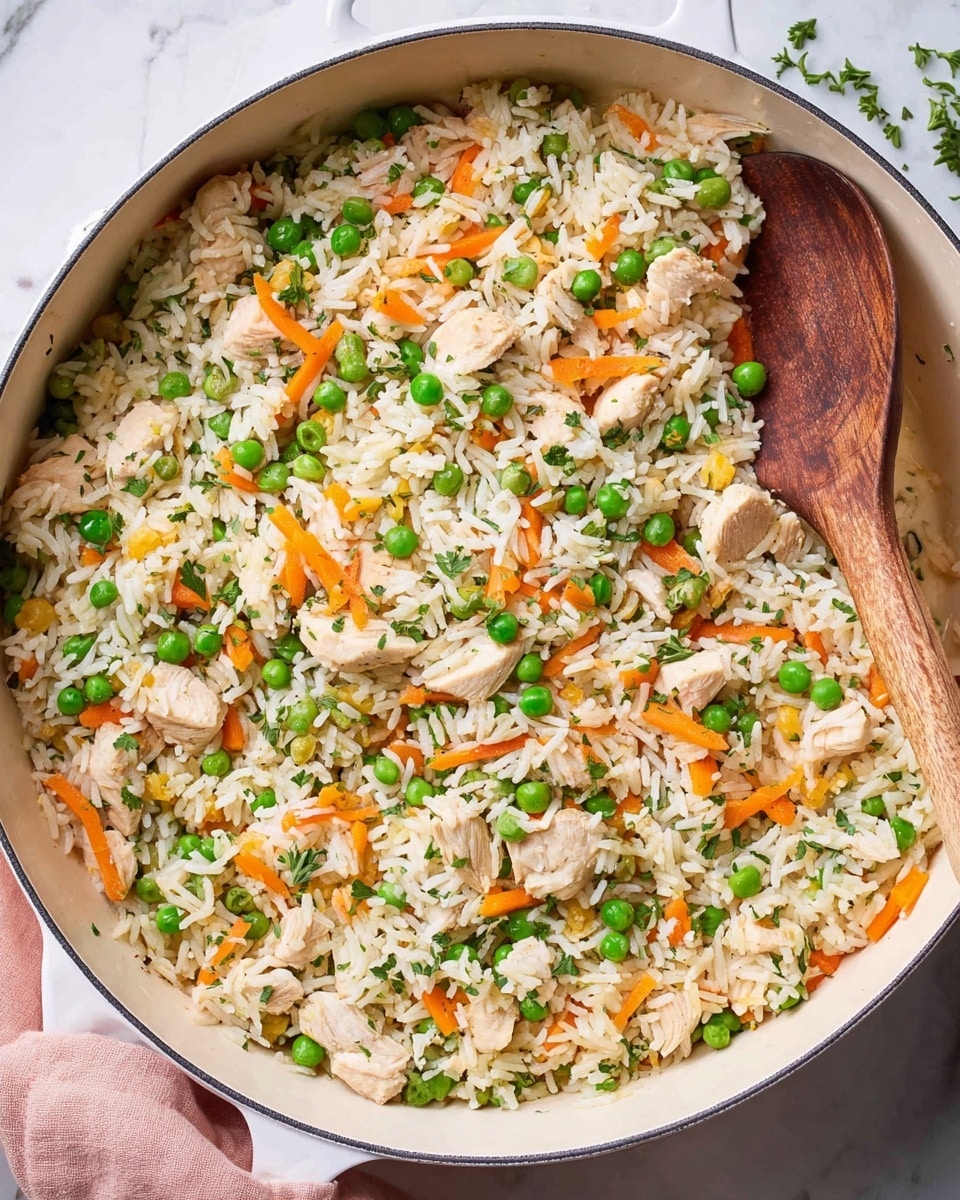 A white deep pan filled with a mix of white rice, small pieces of light cooked chicken, bright green peas, and thin orange carrot strips, all layered evenly. The rice grains look soft and fluffy, mixed well with the colorful vegetables and chicken chunks. Some green herbs sprinkled on top add a fresh touch. A brown wooden spoon resting inside the pan is partially covered by the food. The pan sits on a white marbled surface with a soft pink cloth nearby. photo taken with an iphone --ar 4:5 --v 7
