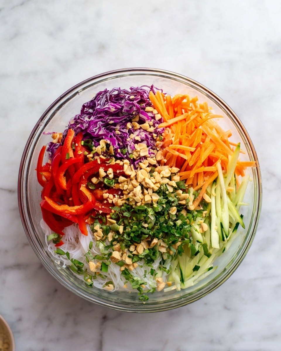 A clear glass bowl is filled with five main layers of colorful fresh vegetables arranged neatly side by side: thin white noodles on the bottom, topped with bright red sliced bell peppers, long thin orange carrot sticks, pale green cucumber sticks, and finely shredded purple cabbage. Chopped green herbs are sprinkled over all layers along with a scattering of crushed light tan peanuts. The bowl sits on a white marbled surface. photo taken with an iphone --ar 4:5 --v 7