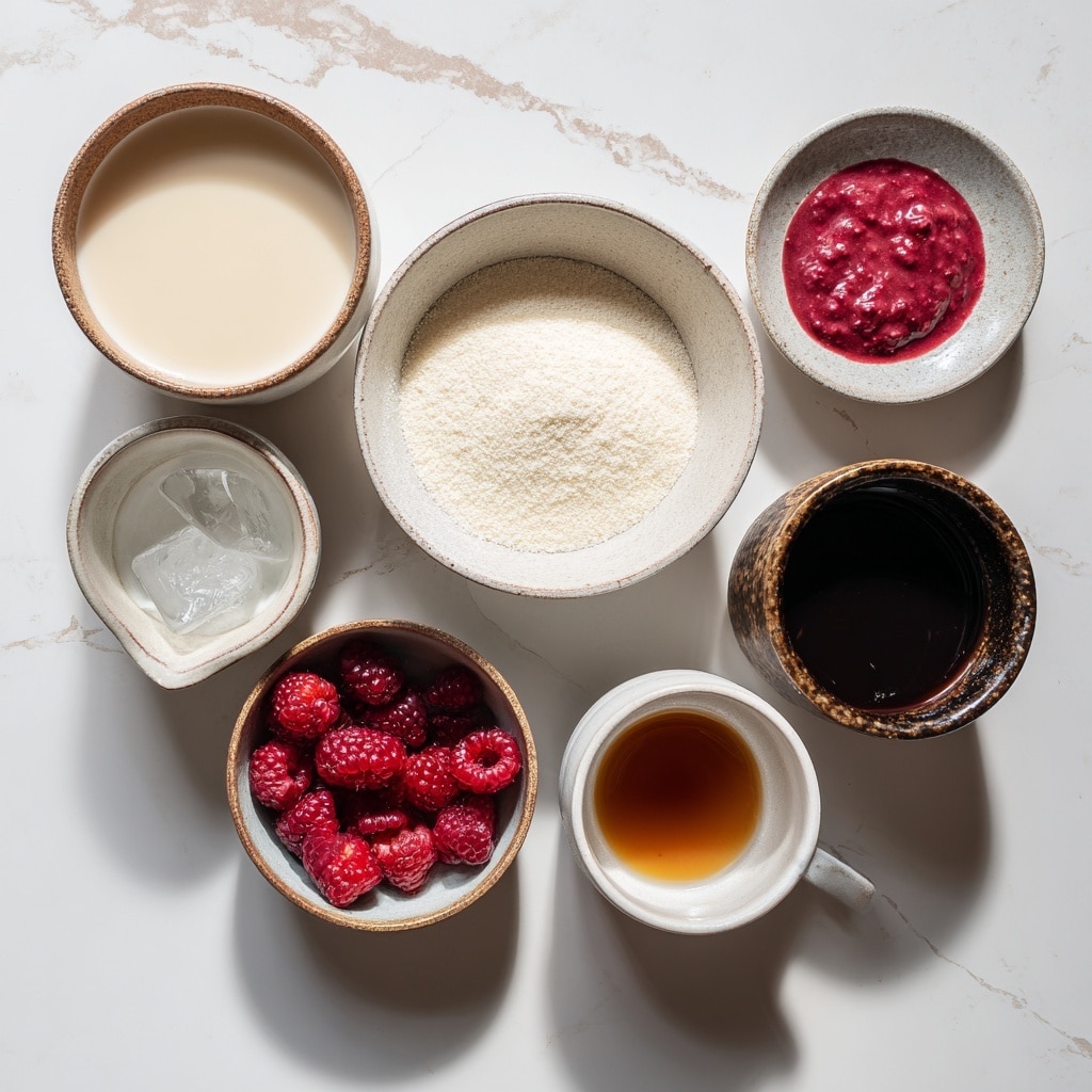 A clear glass filled with a creamy pale pink drink, mixed with small red raspberry pieces spread inside and on top, where three whole raspberries sit, with a shiny metal straw sticking out from the top. The glass is placed on a white marbled surface with a few loose raspberries and coffee beans scattered around. In the background, slightly blurred, there is a white jar with a silver lid containing a similar pink drink and a white bowl filled with more raspberries. photo taken with an iphone --ar 4:5 --v 7