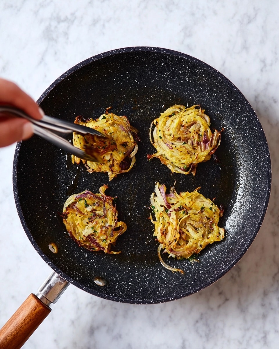 The image shows four small round onion fritters cooking in a black speckled pan with a wooden handle on a white marbled surface. Each fritter is made of thin slices of onion mixed in a yellow batter with specks of green herbs. The fritters have a slightly crispy, browned texture on the outside. On the left side of the image, a woman's hand uses metal tongs to hold one of the fritters. The pan's inside is shiny with some oil visible. photo taken with an iphone --ar 4:5 --v 7