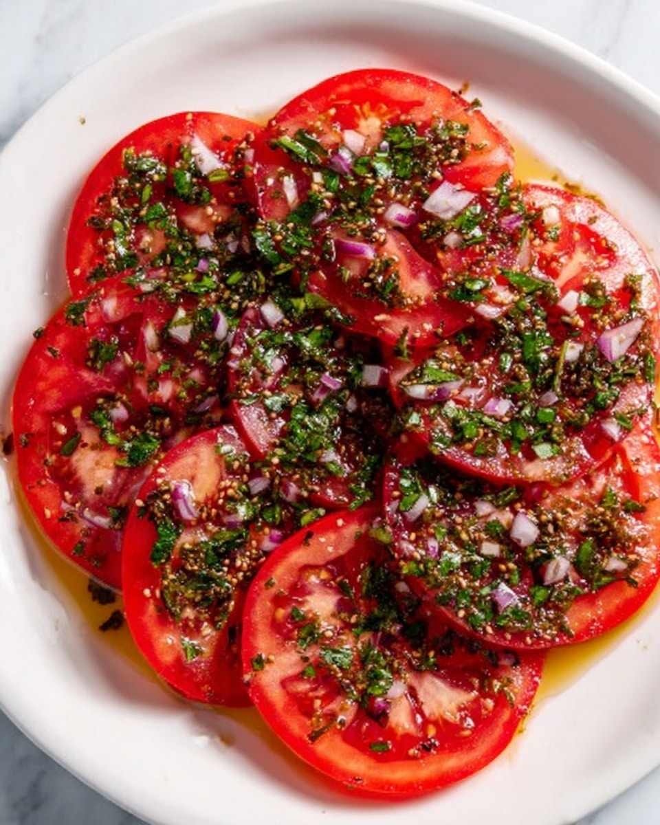 The image shows a white plate with several round slices of bright red tomatoes layered flat, covering almost the entire plate. On top of the tomato slices, there is a fresh green herb mixture sprinkled generously, mixed with small bits of purple onion and light-colored seeds or spices. The surface underneath the plate is a white marbled texture. The colors are vibrant with the red of the tomatoes contrasting with the green and purple herbs, and a slight shine of oil or dressing glistening on top photo taken with an iphone --ar 4:5 --v 7