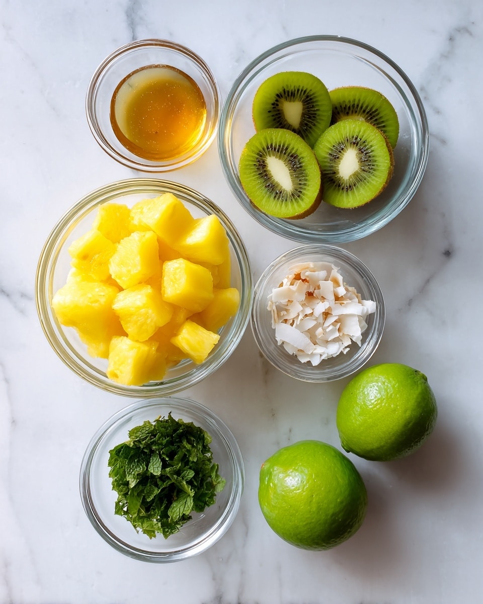The image shows six items arranged neatly on a white marbled surface. On the left, there is a clear glass bowl filled with bright yellow pineapple cubes. At the top center, a clear glass bowl contains slices of green kiwi with the seeds visible. To the right of the kiwi, there is a small clear glass bowl with toasted coconut flakes that are light brown and white. Below the kiwi, a smaller clear glass bowl contains chopped fresh green mint leaves. Below the mint, there is a tiny clear glass bowl of translucent golden honey. To the right of the honey and mint, two whole green limes sit side by side on the surface. The overall look is fresh and colorful, with clear bowls that show off the vibrant colors of the ingredients. Photo taken with an iphone --ar 4:5 --v 7
