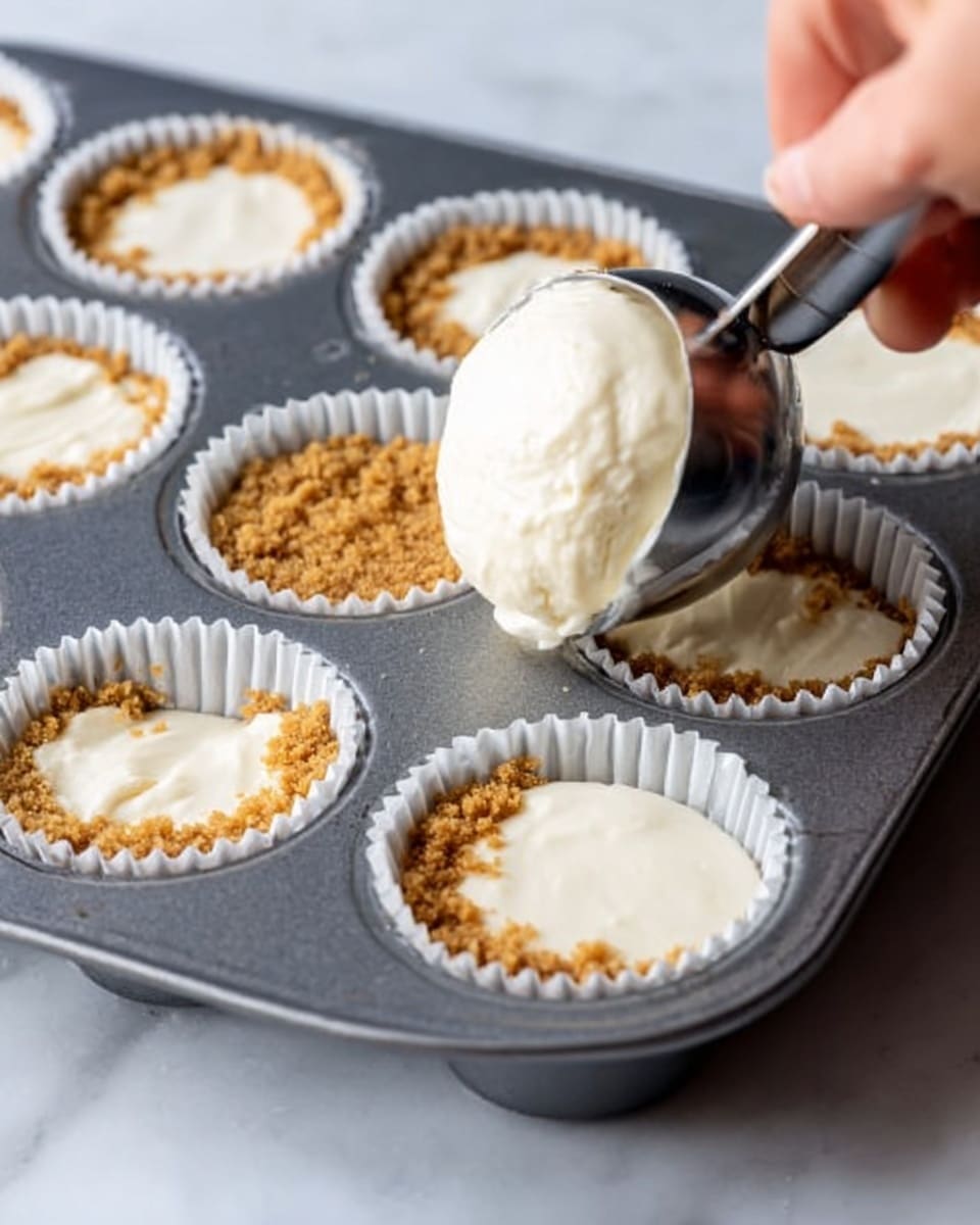 A close-up view of a gray metal muffin tray filled with white paper liners, some lined with a brown crumbly base and others being filled with smooth, creamy white batter from a metal ice cream scoop held by a woman's hand with light skin. The crumbly base looks evenly pressed at the bottom of the liners, while the soft batter is thick and gently poured on top, creating a clear contrast between the crumb layer and the creamy layer above. The background is a white marbled surface. Photo taken with an iphone --ar 4:5 --v 7