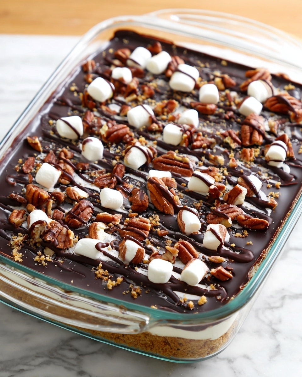 A dessert in a clear glass rectangular dish shows three visible layers: the bottom layer is golden brown and crumbly, the middle layer is a smooth and shiny dark chocolate, and the top layer is decorated with scattered dark brown pecan halves, small white marshmallows, and thin drizzles of dark chocolate sauce creating lines across the surface. The dish is placed on a white marbled texture. photo taken with an iphone --ar 4:5 --v 7