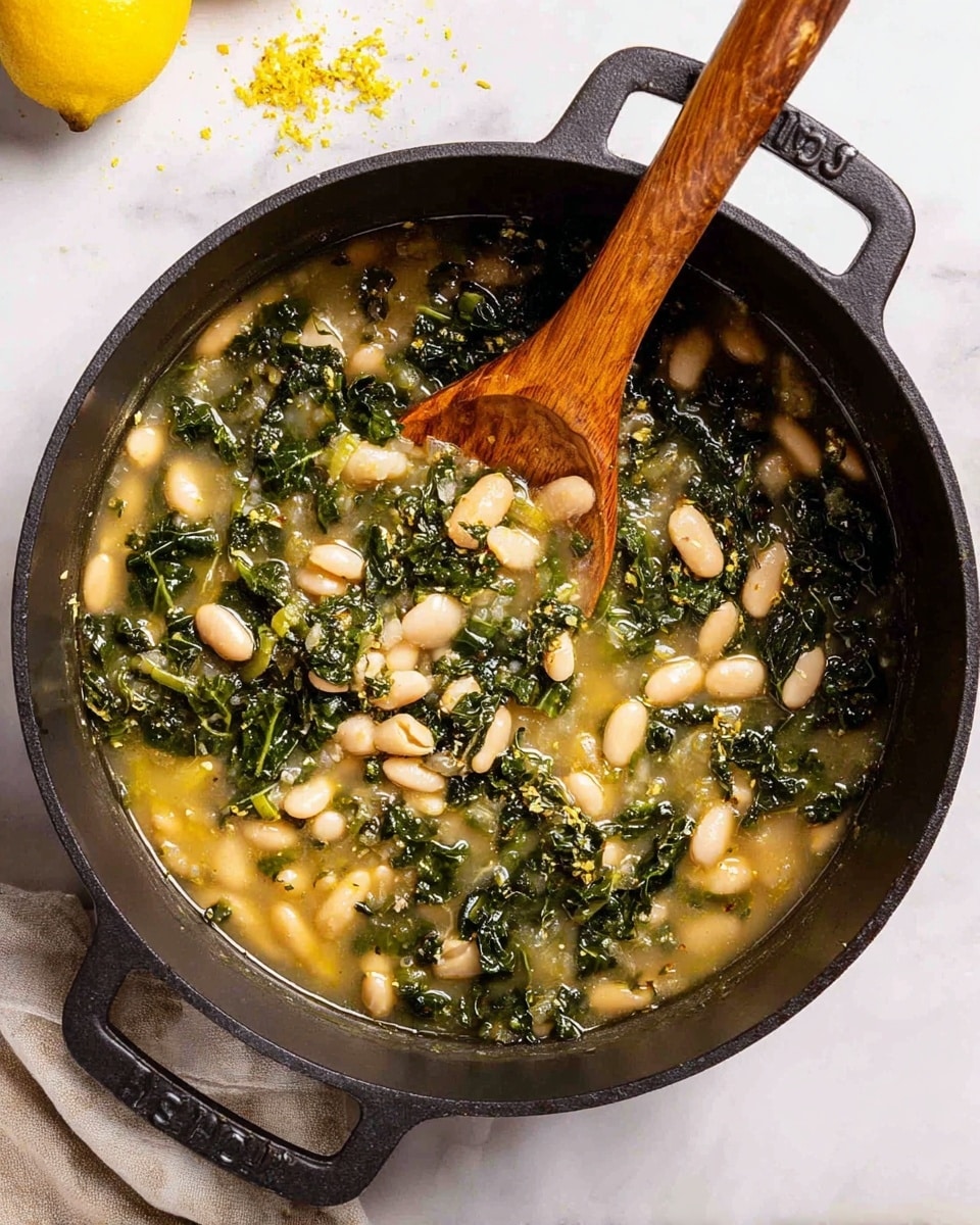 A black pot filled with three main layers: a bottom layer of light yellow broth with small bits of herbs, a middle layer of dark green chopped kale leaves, and a top layer of plump white beans scattered throughout. A wooden spoon with a smooth texture rests inside the pot, partially submerged in the mix, showing the creamy soup's thick consistency. The pot sits on a white marbled surface with a yellow lemon wedge and lemon zest flakes nearby. Photo taken with an iphone --ar 4:5 --v 7