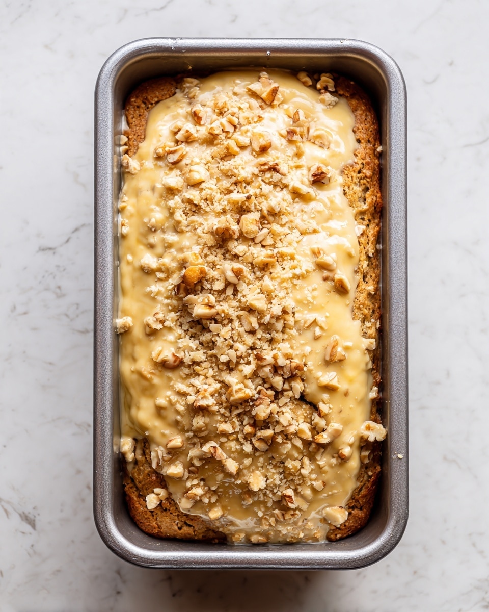 A clear glass bowl full of a thick, pale yellow batter with small banana pieces, topped with a layer of crumbled white flour mixture and nuts. The batter is then mixed, becoming creamy with visible banana bits evenly spread. The batter is poured into a silver loaf pan with straight edges, filling it about halfway. Finally, the baked banana bread shows a golden brown, cracked crust on top, still inside the same loaf pan, all placed on a white marbled surface. photo taken with an iphone --ar 4:5 --v 7