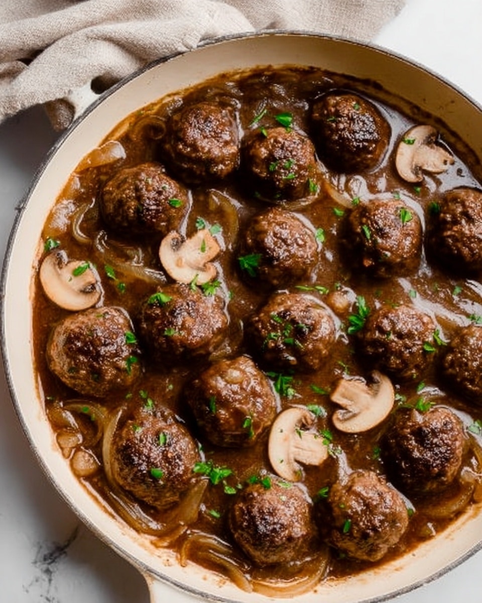The image shows a white skillet filled with dark brown meatballs in a rich brown sauce. There are about nine round meatballs evenly spread across the pan. Thinly sliced light beige mushrooms float in the sauce among the meatballs. Some thin, translucent onion slices are mixed with the sauce, adding texture. Small green herb pieces are sprinkled over the dish, adding a touch of color contrast. The skillet sits on a white marbled surface with a soft fabric towel partially visible at the top. A woman's hand holds the skillet handle from the left side. photo taken with an iphone --ar 4:5 --v 7