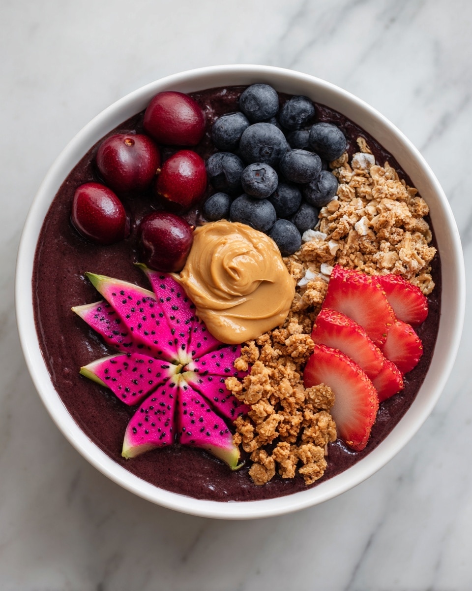 A white bowl filled with a smooth dark purple smoothie base creates the first layer, spread evenly at the bottom. On this base, there are neat sections of fresh fruits and toppings: a cluster of deep red cherries halved on the left, bright red raspberries just below, a pile of golden brown granola sprinkled twice in the top right and middle-left areas, a rich dollop of creamy light brown peanut butter placed centrally, a bunch of plump dark blue blueberries above the peanut butter, vibrant pink dragon fruit shaped in flower-like pieces below the peanut butter, and two large red strawberries with their green tops on the far right slightly sliced. The bowl sits on a white marbled surface. The photo taken with an iphone --ar 4:5 --v 7
