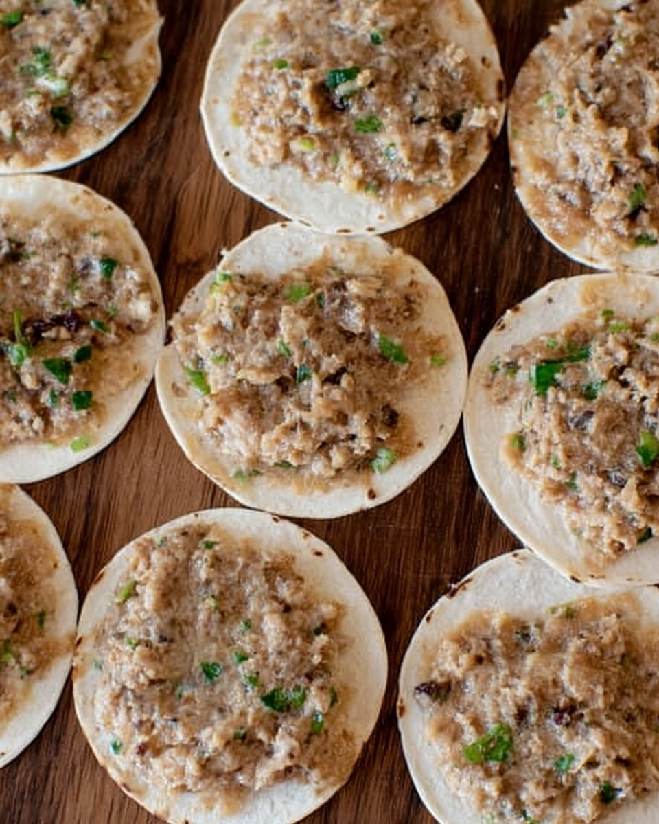 Several small white tortillas each topped with a thin layer of light brown, slightly chunky mixture with visible small pieces of darker bits and bits of green, arranged closely on a wooden surface. The mixture looks spread unevenly on each tortilla, covering most of the top. The overall colors are light brown, beige, hints of green, and white from the tortillas. Photo taken with an iphone --ar 4:5 --v 7