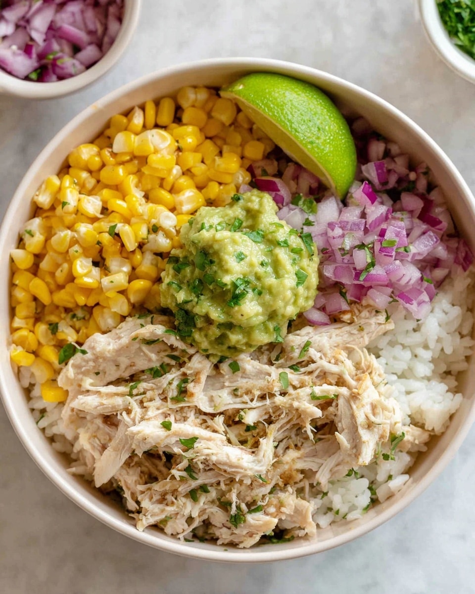 A white bowl filled with four main layers arranged side by side: yellow corn kernels, chopped purple-red onions, shredded light beige chicken mixed with small green herb bits, and soft off-white rice. On top of the rice and near the chicken sits a scoop of green guacamole with a slightly chunky texture. A wedge of bright green lime rests on the shredded chicken. In the background is a small white bowl of finely chopped red onions, and the whole setting is on a white marbled surface. Photo taken with an iphone --ar 4:5 --v 7