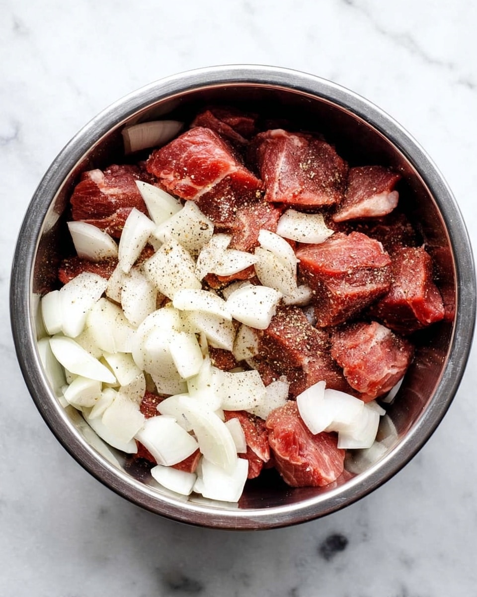 A metal bowl with thick pieces of raw red meat at the bottom, sprinkled with black pepper and seasoning. On top of the meat are large white onion pieces, roughly chopped and scattered evenly, filling about half of the bowl. The bowl is placed on a white marbled surface. Photo taken with an iphone --ar 4:5 --v 7