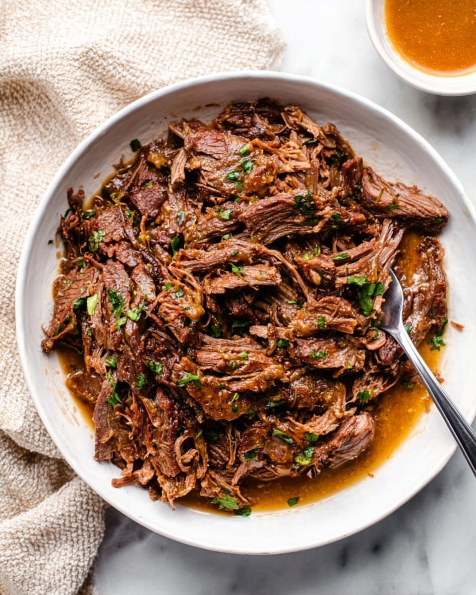 A white bowl filled with shredded dark brown meat that looks tender and juicy, with small bits of green herbs scattered throughout. The meat is mixed with a light brown sauce that adds shine and moisture to the dish. A metal fork is placed on the right side inside the bowl, partly under the meat. The bowl sits on a white marbled surface with a light beige textured cloth partially visible on the top left corner and a small bowl with an orange-brown sauce on the top right edge of the image photo taken with an iphone --ar 4:5 --v 7