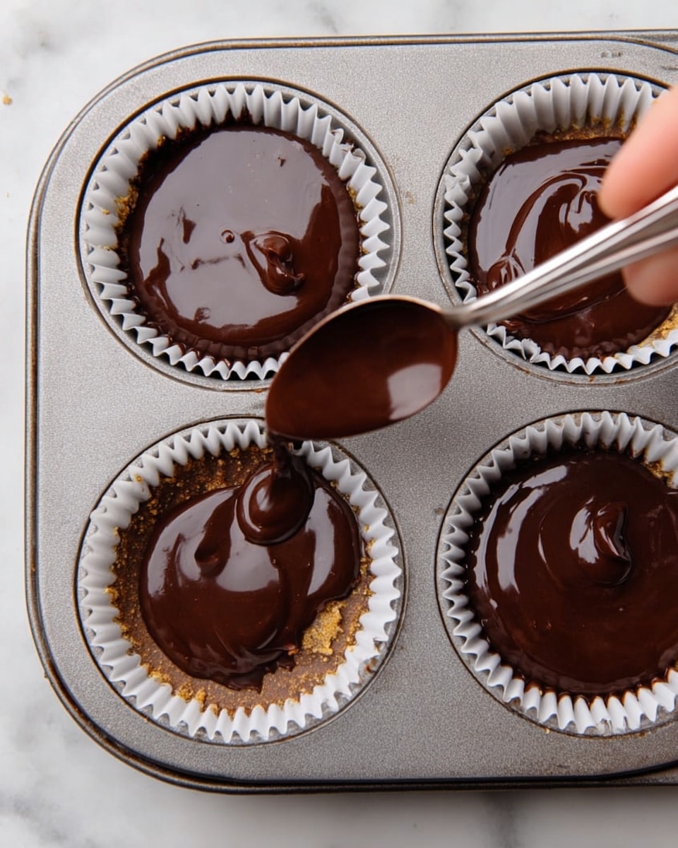 A close-up top view of a metal muffin tray with four white paper liners filled with three smooth, dark brown chocolate layers on top. A woman's hand is holding a spoon with glossy chocolate, pouring it carefully into the last liner, making a shiny, thick top layer. The background is a white marbled texture. photo taken with an iphone --ar 4:5 --v 7