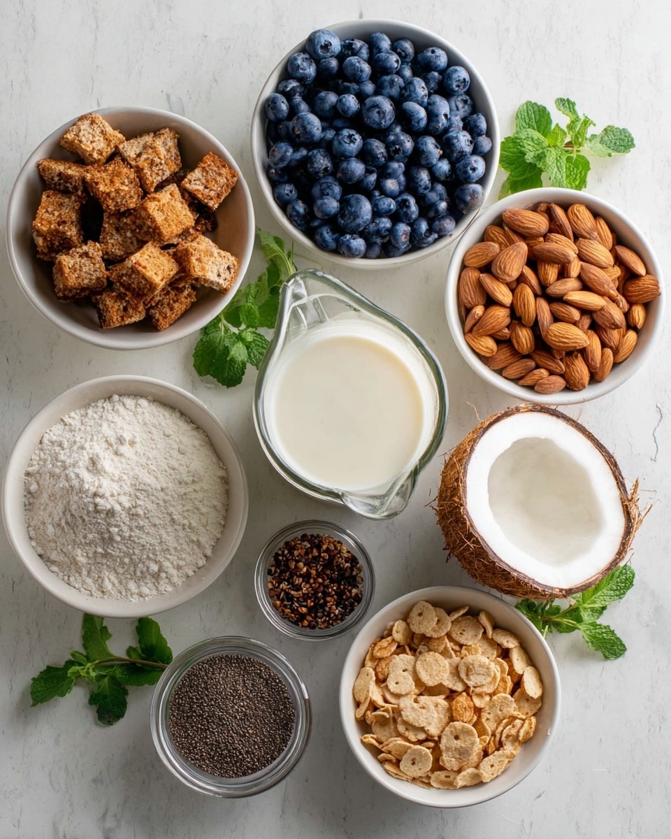 The image shows eight white bowls arranged on a white marbled surface. The top left bowl holds brown toasted bread cubes with a rough texture. To its right, a bowl is filled with smooth, whole brown almonds. Below the bread cubes, a bowl is full of round, plump blueberries in dark blue shades. Centered is a clear glass pitcher with fresh white milk. To the right of the pitcher, there is a halved coconut shell showing its white inner flesh and brown rough outer shell. Below the pitcher, a bowl contains fine white flour. To the bottom left, there is a small jar with tiny black seeds next to a bowl holding ground dark brown powder. Lastly, the bottom right bowl has light brown round cereal flakes with a crunchy texture. Some fresh green mint leaves are placed near the coconut, completing the arrangement. photo taken with an iphone --ar 4:5 --v 7