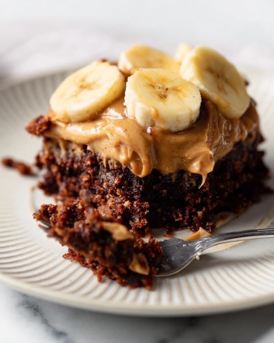 A close-up of a dessert on a white plate with ridged edges, placed on a white marbled surface. The dessert has three main layers: the bottom layer is dark brown and crumbly with a rough texture, the middle layer is a smooth light brown spread like peanut butter, and the top layer consists of thick, round slices of yellow banana. A silver fork rests on the plate near the dessert with some of the dark crumbly layer stuck to its prongs. A woman's hand holding the fork is partially visible. Photo taken with an iphone --ar 4:5 --v 7