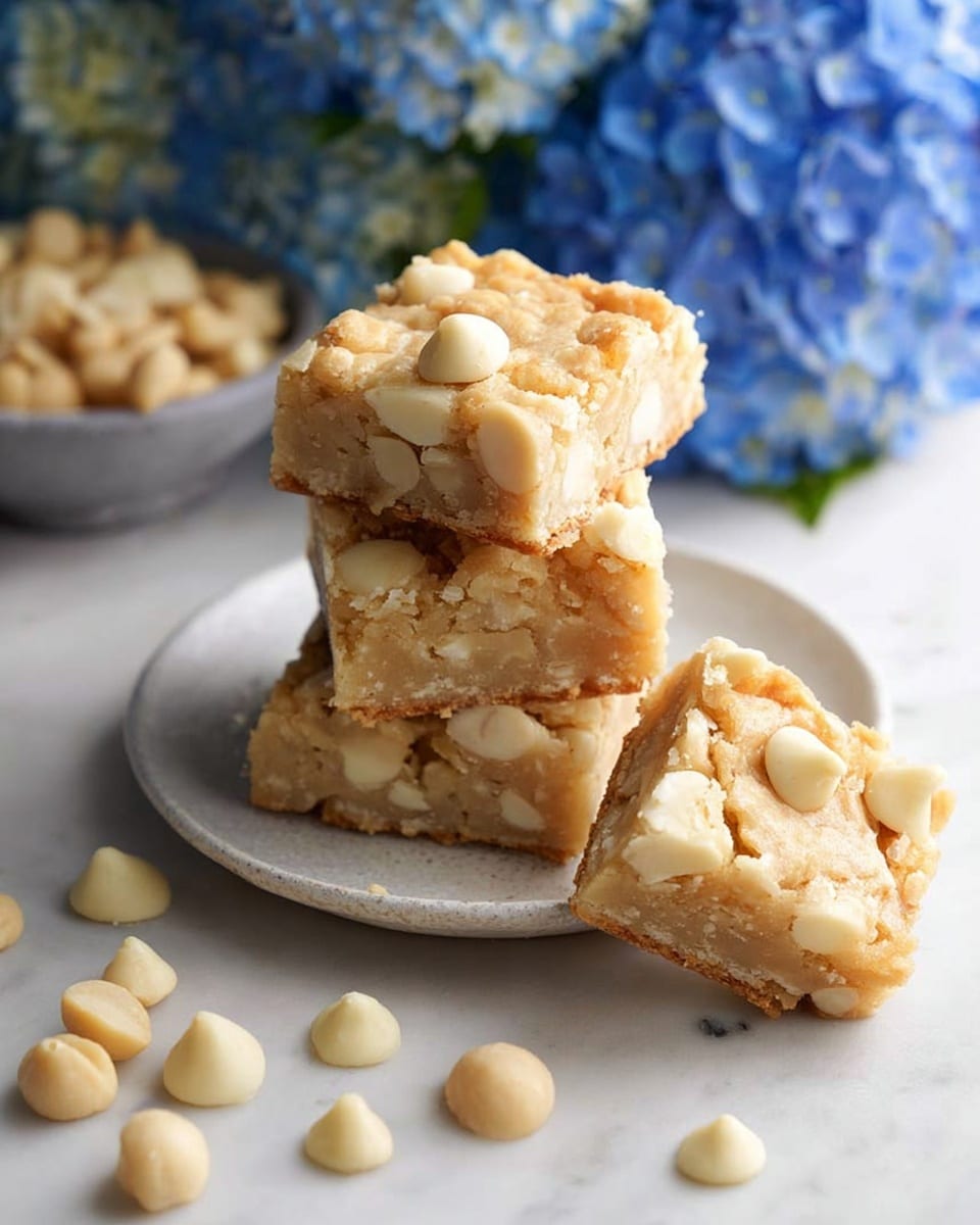A stack of four square bars sits on a small white plate with a matte finish, each bar light beige with visible chunks of macadamia nuts and white chocolate chips embedded throughout. The bars appear soft with a slightly crumbly texture, and one bar lies flat in front of the stack, showing its uneven top layer filled with larger and smaller nut pieces. Scattered around the plate and the surface are round, pale macadamia nuts and creamy white chocolate chips. The scene is set on a white marbled table, with a blurred small bowl of macadamia nuts in the background and a large pot of bright blue hydrangea flowers adding a soft touch on the left. The lighting is natural and bright, enhancing the creamy colors of the bars and nuts. photo taken with an iphone --ar 4:5 --v 7