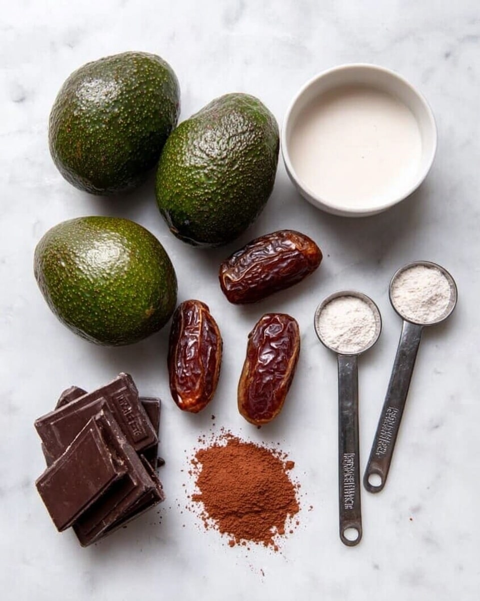 The image shows three whole dark green avocados with bumpy skin lined up left to right, above three brown dates placed side by side. To the right, a white bowl filled with white liquid sits next to two metal measuring spoons with white powder inside, arranged neatly on a white marbled surface. Below the bowl and spoons, a small pile of brown cocoa powder rests beside two small, stacked dark chocolate bars. The overall layout is clean and simple, with ingredients spaced out evenly and clearly visible. Photo taken with an iphone --ar 4:5 --v 7