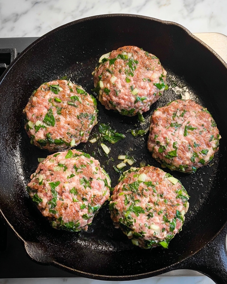 The image shows five uncooked patties placed in a black cast iron pan on a stove. Each patty is round and thick, with a pinkish base mixed with visible small pieces of green leafy herbs and white onion bits spread throughout. The patties have a rough, uneven texture with herbs and onion scattered both on the surface and inside, giving a fresh, mixed look. The cast iron pan has a slightly shiny, oily surface indicating heat, and the stove beneath has a steel grey color. The background features a white marbled texture. Photo taken with an iphone --ar 4:5 --v 7