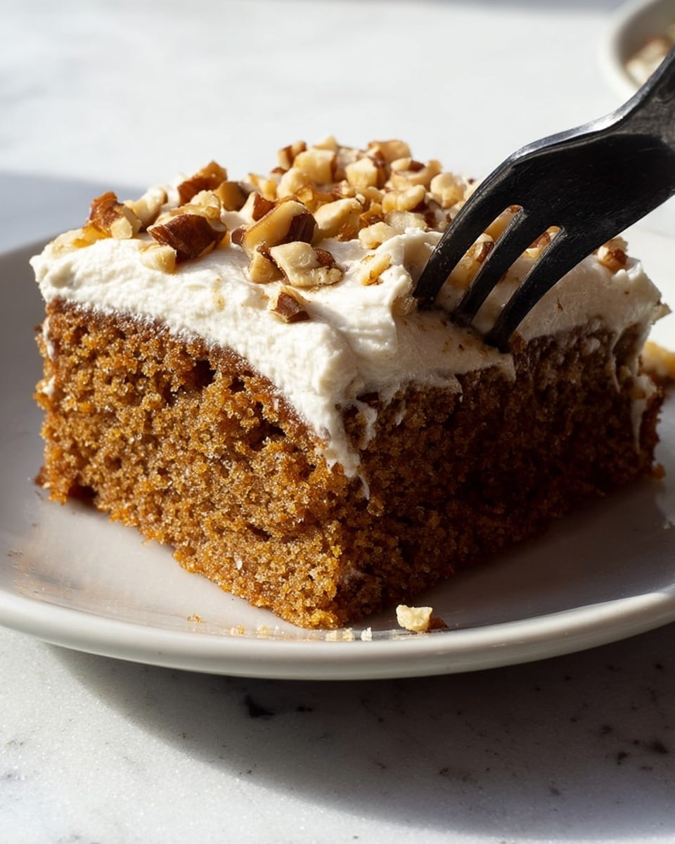A close-up image of a single square piece of moist brown cake with a soft, spongy texture on a white plate. The top layer is thick white frosting, smooth and creamy, sprinkled with chopped nuts that add a rough texture. A black fork is digging into the cake from the right side, emphasizing the softness of the cake and frosting. The plate is set on a white marbled surface with bright, natural lighting highlighting the detailed textures of the cake and nuts. Photo taken with an iphone --ar 4:5 --v 7