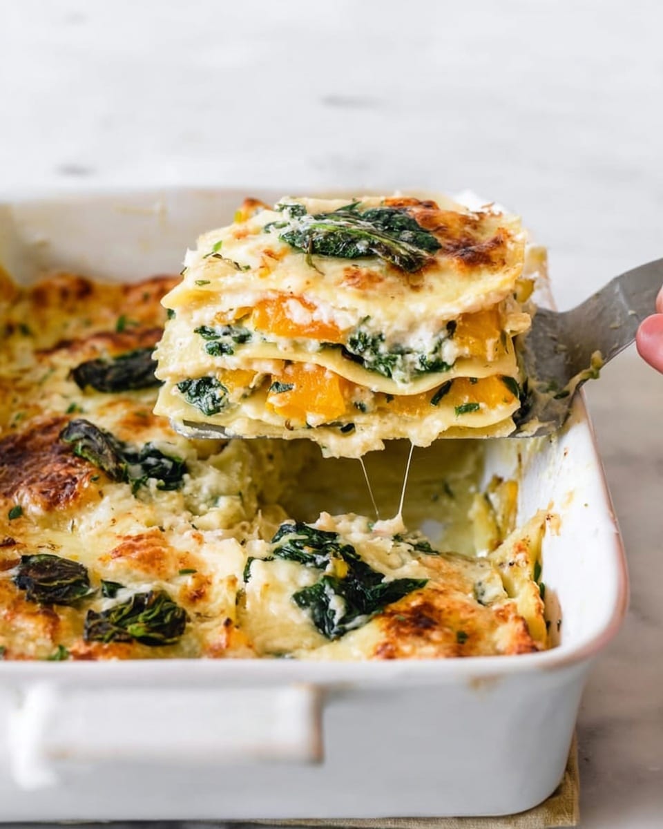 A white rectangular baking dish holds a layered lasagna with creamy, light yellow cheese sauce and green spinach leaves on top and inside. The slice on the spatula lifted by a woman's hand shows clear layers of thin, soft pasta, orange squash, white cheese, and dark green spinach, all mixed with melted cheese and a slightly golden baked top. The dish sits on a white marbled surface with hints of melted cheese stretching slightly between the lasagna and the spatula. Photo taken with an iphone --ar 4:5 --v 7