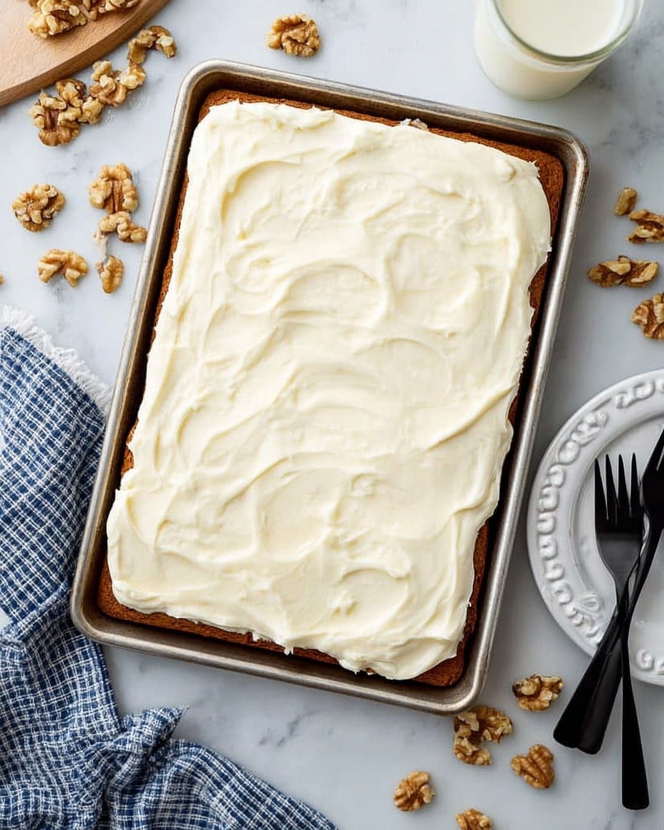 A rectangular cake sits in a metal baking tray on a white marbled surface, with one thick layer of light brown cake at the bottom and a thick, smooth layer of white frosting spread evenly on top, showing gentle swirls and soft textures. To the right, there is a white plate with a scalloped edge and two black forks resting on it. Pieces of walnuts are scattered around, and a glass of milk is partially visible in the top right corner. A woman's hand towel with blue and white checks is placed near the bottom left. Photo taken with an iphone --ar 4:5 --v 7