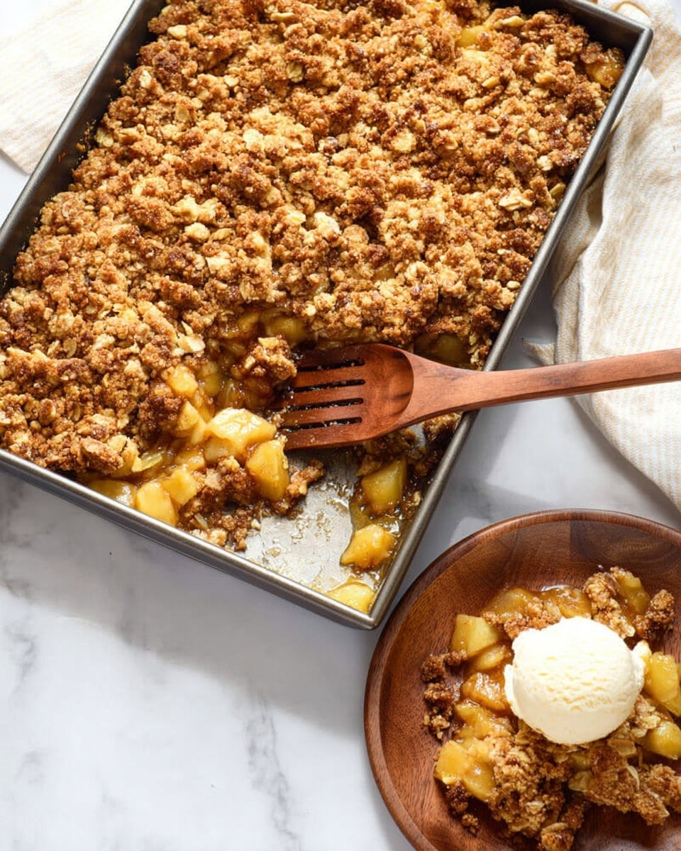 A rectangular metal baking pan filled with a crumb-topped dessert, showing two clear layers: a bottom layer of soft, slightly golden yellow chunks mixed with syrup, and a rough, light brown crumb layer with oats on top, the crumbs evenly spread and textured. A wooden slotted spoon rests inside the pan partly on top of the crumb layer with some crumb and syrup on it. Below the pan on a white marbled surface is a round wooden plate holding a serving of the dessert with a scoop of creamy white ice cream on top. Photo taken with an iphone --ar 4:5 --v 7
