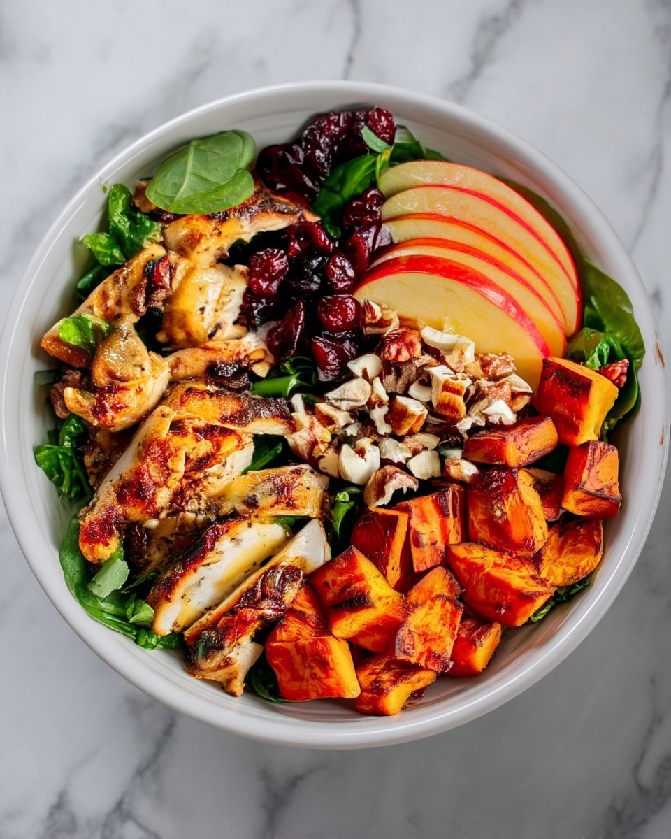 A white bowl sits on a white marbled surface filled with a colorful layered dish. The bottom layer is fresh green leafy spinach covering the base. Sliced grilled chicken with a golden brown outside and grill marks is arranged neatly on one side. Next to the chicken are small orange cubes of roasted sweet potatoes with light charring. Thinly sliced red apple pieces with smooth texture fan out next to the sweet potatoes. A cluster of dried dark red cranberries is placed in the center near the chicken, and a small pile of chopped nuts with white and light brown tones sits just below the cranberries. The dish looks fresh and vibrant with a mix of soft, crunchy, and tender textures. Photo taken with an iphone --ar 4:5 --v 7