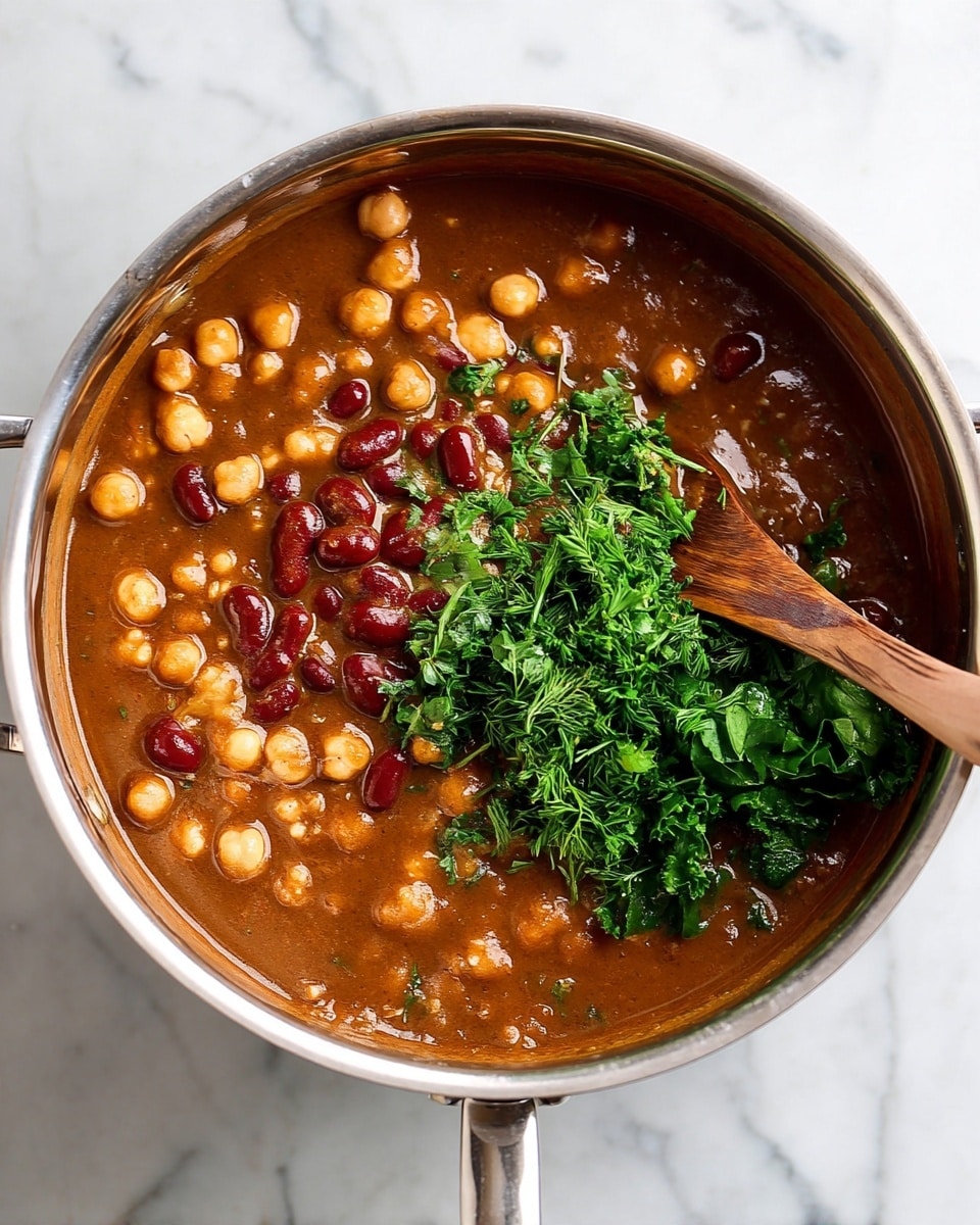 A large silver pot filled with a thick brown stew that has visible chickpeas, small red beans, and green leafy herbs layered on one side. A wooden spoon is partially submerged, mixing the greens and beans in the stew. The pot is placed on a white marbled surface. Photo taken with an iphone --ar 4:5 --v 7